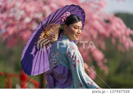 woman in yukata (kimono dress) holding umbrella with sakura flower or cherry blossom blooming in garden woman in yukata (kimono dress) holding umbrella with sakura flower or cherry blossom blooming in garden 137487588
