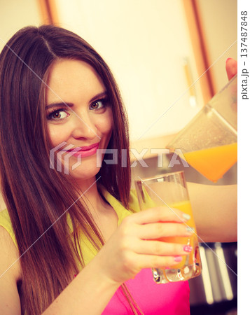 Woman make orange juice in juicer machine pouring drink in glass 137487848