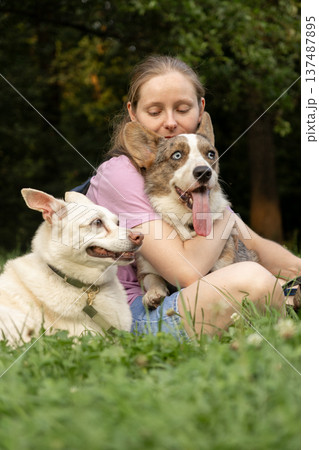 Professional dog walker young woman with pack of dogs is sitting on grass and enjoying walk animals. 137487895