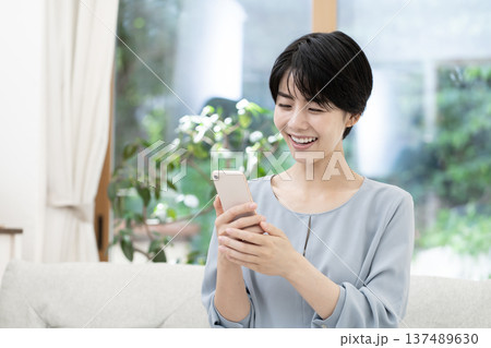 ソファーに座りスマートフォンを使う若い女性 ソファーに座りスマートフォンを使う若い女性 137489630