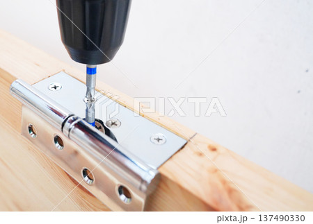 Screwdriver is used to attach hinge to wooden door frame. Screwdriver is used to attach hinge to wooden door frame. 137490330