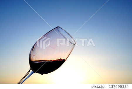 Red Wine Swirling background. Vibrant red wine is splashing out glass, creating droplets on blue sky Red Wine Swirling background. Vibrant red wine is splashing out glass, creating droplets on blue sky 137490384