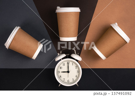 Disposable paper cups and white alarm clock on paper background, top view. 137491092