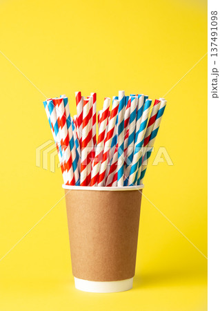Disposable paper cup with striped paper straws on a yellow background. 137491098