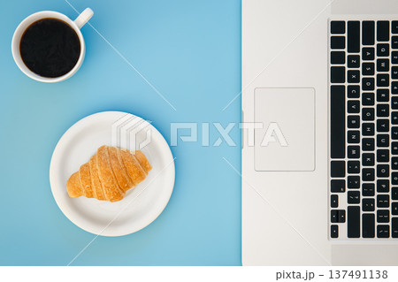 Croissant, cup of coffee and laptop on a blue background, flat lay. Croissant, cup of coffee and laptop on a blue background, flat lay. 137491138