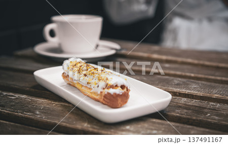 Cup of coffee and eclair on a wooden table close-up. 137491167
