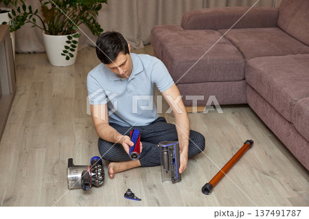 Man sitting on floor assembling parts of a vacuum cleaner 137491787
