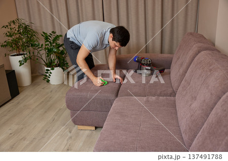 Man cleaning sofa upholstery at home using a powerful handheld vacuum cleaner 137491788