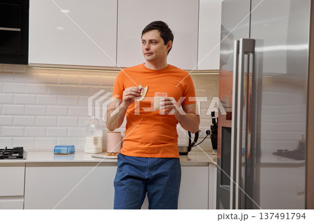 Young man standing in a modern kitchen, eating a sandwich and drinking milk Young man standing in a modern kitchen, eating a sandwich and drinking milk 137491794