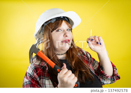 Woman wearing hard hat holding hammer and nail Woman wearing hard hat holding hammer and nail 137492578
