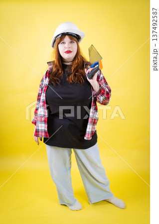 Young woman builder wearing hard hat holding trowel Young woman builder wearing hard hat holding trowel 137492587