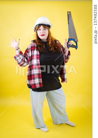 Woman wearing hard hat holding saw ready for work Woman wearing hard hat holding saw ready for work 137492588