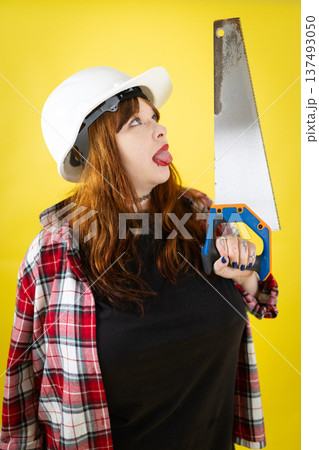 Woman with hard hat playing with hand saw Woman with hard hat playing with hand saw 137493050