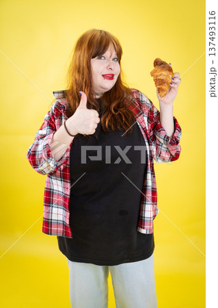 Young woman enjoying croissant giving thumbs up gesture 137493116