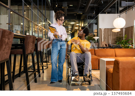 Businesswoman holding folders discussing with disabled man in shared workspace Businesswoman holding folders discussing with disabled man in shared workspace 137493684