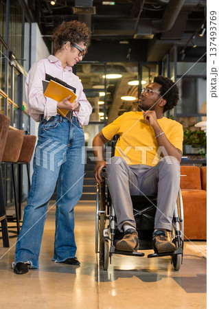 Woman holding documents and man in wheelchair communicating standing in coworking interior 137493769