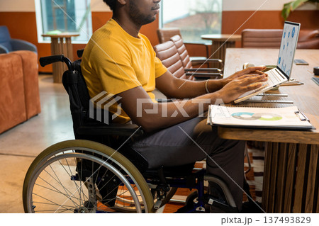 Man in wheelchair with coffee mug using laptop computer in coworking interior Man in wheelchair with coffee mug using laptop computer in coworking interior 137493829