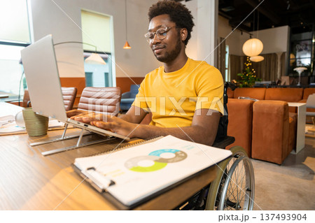 Man in wheelchair working on laptop with online business data in coworking space 137493904