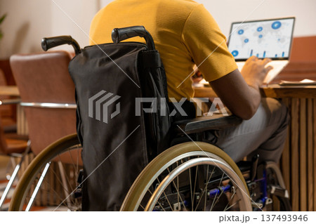 Disabled man in wheelchair typing on laptop computer analyzing world migration statistics Disabled man in wheelchair typing on laptop computer analyzing world migration statistics 137493946