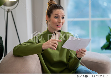 Woman in green blouse and jeans sitting on the sofa with a paper in hands Woman in green blouse and jeans sitting on the sofa with a paper in hands 137494102