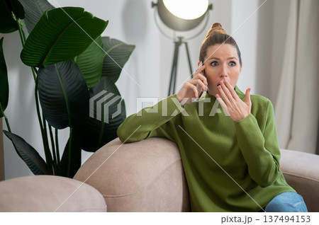 Woman in green sitting on the sofa and having a phone call 137494153