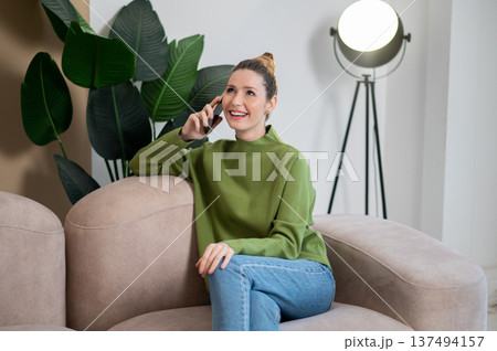 Woman in green sitting on the sofa and having a phone call 137494157