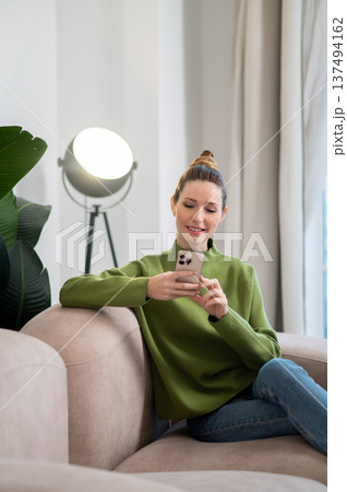 Woman in green sitting on the sofa and having a phone call 137494162