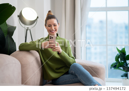 Woman in green sitting on the sofa and having a phone call Woman in green sitting on the sofa and having a phone call 137494172