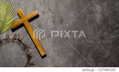 A wooden cross, a crown of thorns, and a palm leaf symbolize the Passion of Christ and Holy Week. Set on a dark stone background with copy space for Easter and Good Friday themes A wooden cross, a crown of thorns, and a palm leaf symbolize the Passion of Christ and Holy Week. Set on a dark stone background with copy space for Easter and Good Friday themes 137495287