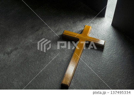 Simple wooden Christian cross on a dark textured surface, dramatically illuminated by a bright shaft of light from a doorway, symbolizing faith, hope, and spiritual light in the darkness Simple wooden Christian cross on a dark textured surface, dramatically illuminated by a bright shaft of light from a doorway, symbolizing faith, hope, and spiritual light in the darkness 137495334