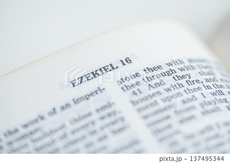 A selective focus macro shot of an open Bible page featuring the chapter title Ezekiel 16, showing text details with a shallow depth of field A selective focus macro shot of an open Bible page featuring the chapter title Ezekiel 16, showing text details with a shallow depth of field 137495344