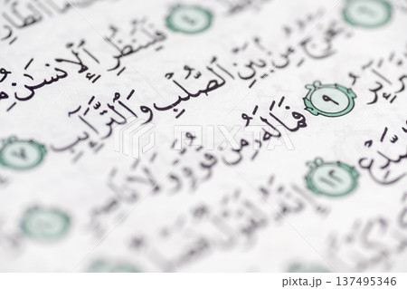 A macro shot focusing on verses from the Holy Quran, written in traditional Arabic script with decorative green verse markers on a white page A macro shot focusing on verses from the Holy Quran, written in traditional Arabic script with decorative green verse markers on a white page 137495346