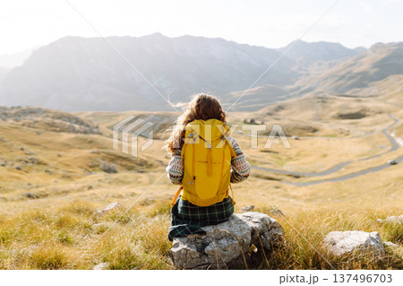 Traveler woman with a bright yellow backpack strolls through golden meadows. Active lifestyle Traveler woman with a bright yellow backpack strolls through golden meadows. Active lifestyle 137496703