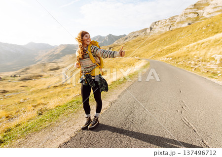 Hitchhiking woman traveler try to stop car on the mountain road. Travel and vacation theme 137496712