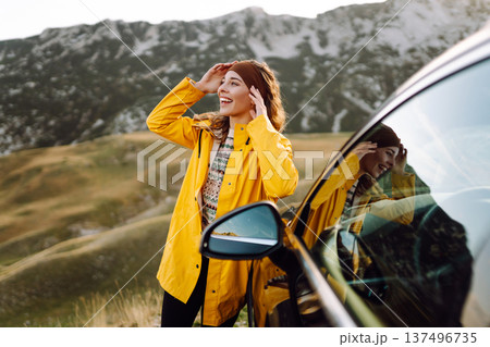 A cheerful traveler enjoying a scenic mountain view while sitting on the trunk. Travelling by car. 137496735