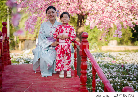 woman and child girl in yukata (kimono dress) on red bridge with sakura flower or cherry blossom blooming in garden 137496773