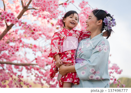 woman and child girl in yukata (kimono dress) with sakura flower or cherry blossom blooming in garden woman and child girl in yukata (kimono dress) with sakura flower or cherry blossom blooming in garden 137496777