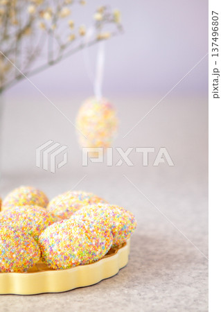 Colorful pastel Easter eggs covered in sprinkles on a yellow plate with soft background 137496807