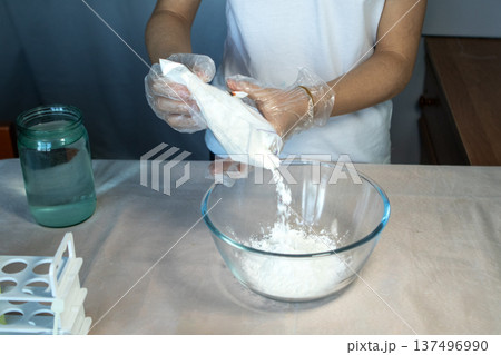 Close-up of gloved hands pouring a white substance into a glass bowl. 137496990