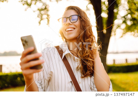 Happy woman enjoying sunset on the embankment with phone in her hands. City life concept. Happy woman enjoying sunset on the embankment with phone in her hands. City life concept. 137497147