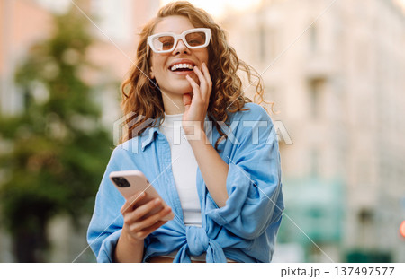 Portrait happy woman walking with phone in city. Online Communication with friend. Lifestyle concept Portrait happy woman walking with phone in city. Online Communication with friend. Lifestyle concept 137497577