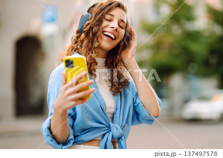 Happy relaxed woman in wireless headphones choosing, listening favorite music in urban city street. Happy relaxed woman in wireless headphones choosing, listening favorite music in urban city street. 137497578