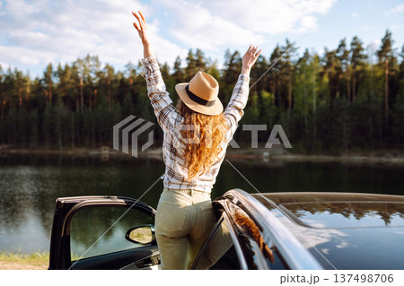 Joyful traveler embraces nature at sunset by lakeside with open car door, freedom, adventure. Joyful traveler embraces nature at sunset by lakeside with open car door, freedom, adventure. 137498706