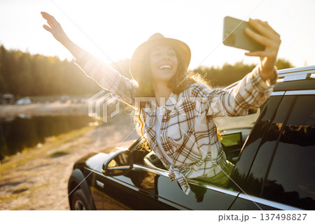 Happy woman on vacation taking selfie photo with smartphone near car. Stylish model on a car trip. 137498827