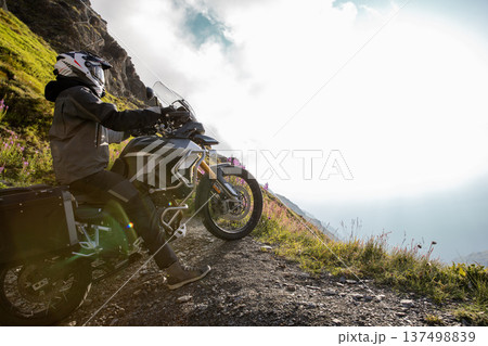 Motorcycle rider posing in Italian Alps during sunrise, dramatic sky. Travel and freedom, outdoor activities 137498839