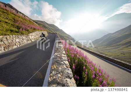 Motorcycle rider riding in Italian Alps during sunrise, dramatic sky. Travel and freedom, outdoor activities 137498841