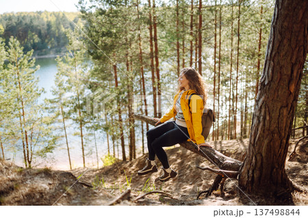 A cheerful young woman in a yellow jacket enjoying a sunny day by the lake. Trips. Active lifestyle. 137498844