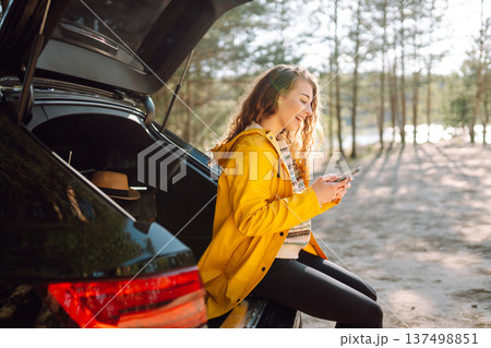 Young woman sitting in open trunk with phone. Lifestyle, travel, tourism, nature, active life. Young woman sitting in open trunk with phone. Lifestyle, travel, tourism, nature, active life. 137498851