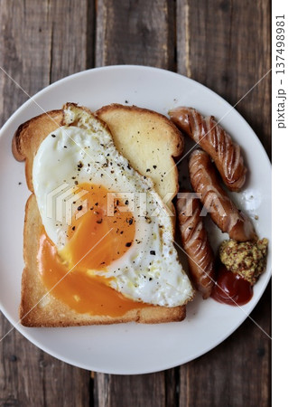 半熟目玉焼きを崩して乗せたトーストと粗挽きウインナー 137498981