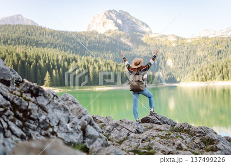 Back view young woman with backpack looking the view of the mountain lake in sunny weather. 137499226